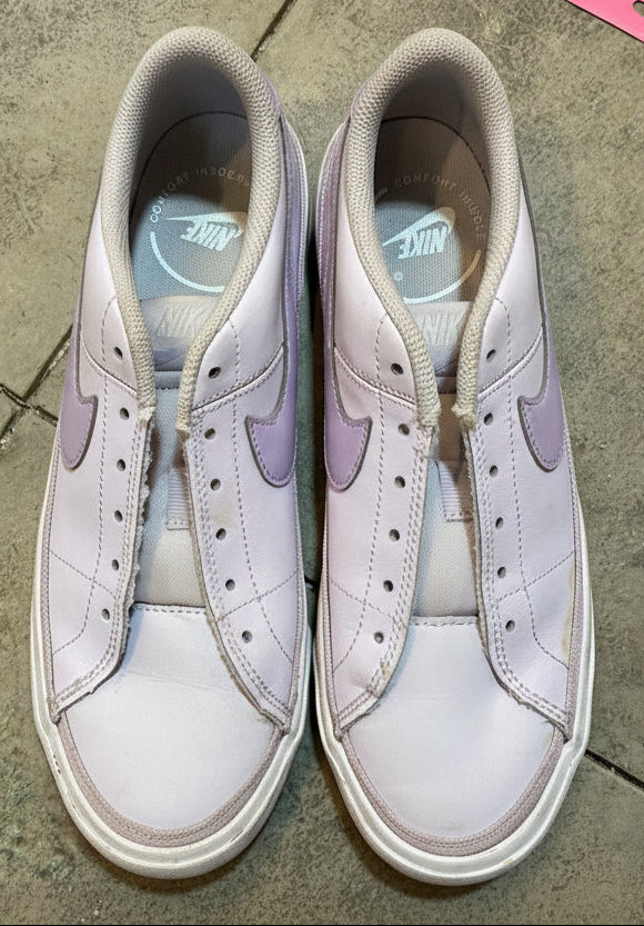 Pair of white sneakers with purple swoosh logo on a concrete floor.