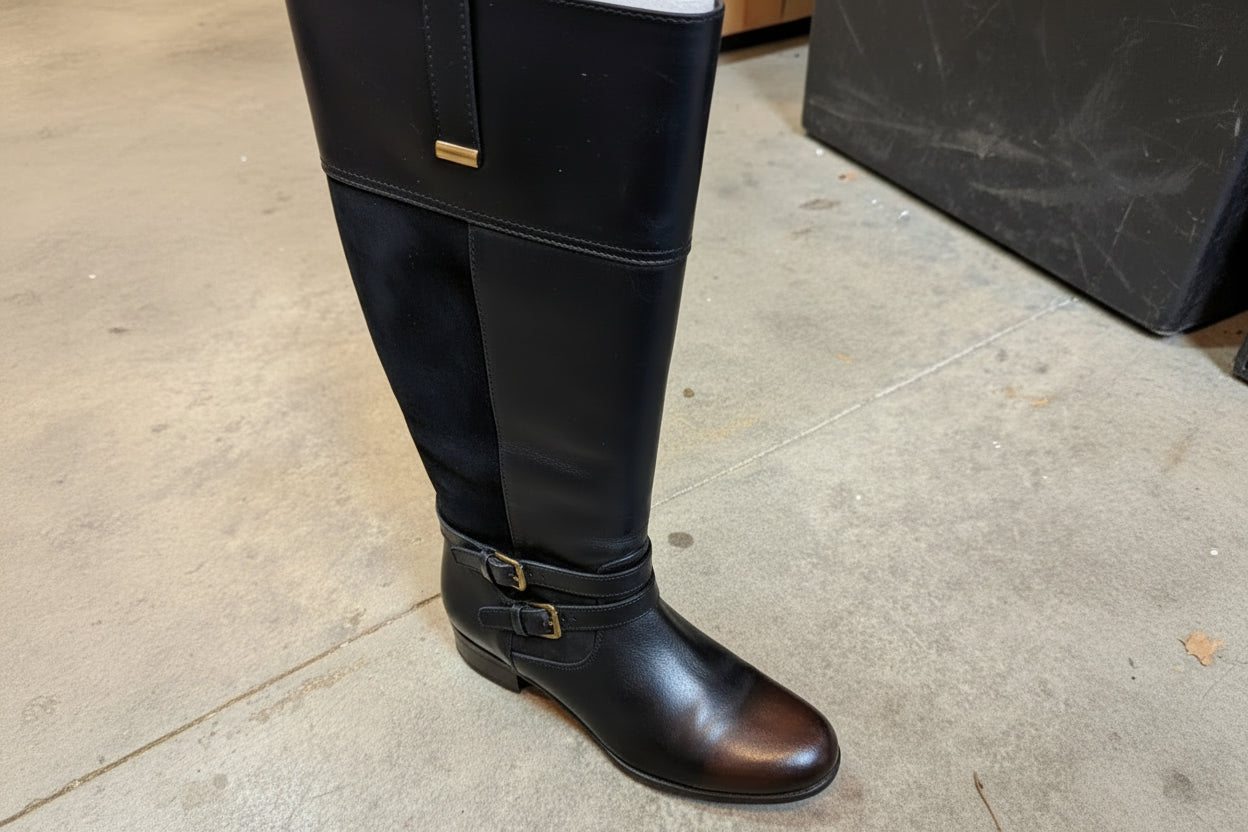 Pair of black riding boots on a textured surface